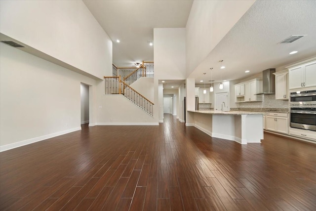 kitchen with hanging light fixtures, dark wood-type flooring, wall chimney range hood, and a high ceiling