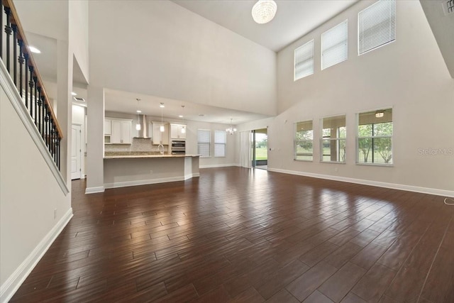 unfurnished living room featuring a towering ceiling, dark hardwood / wood-style floors, and a healthy amount of sunlight