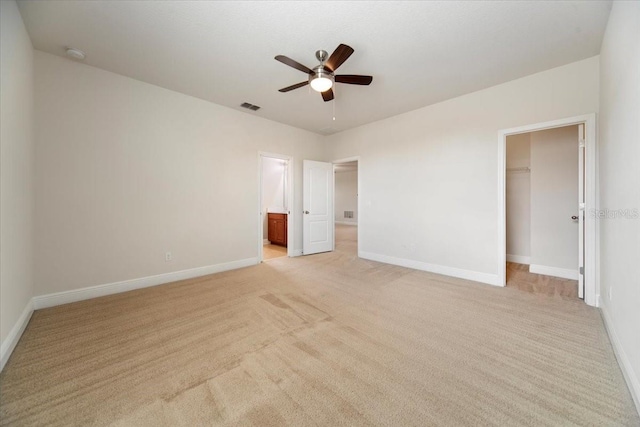 unfurnished bedroom featuring a closet, ceiling fan, a walk in closet, ensuite bathroom, and light carpet