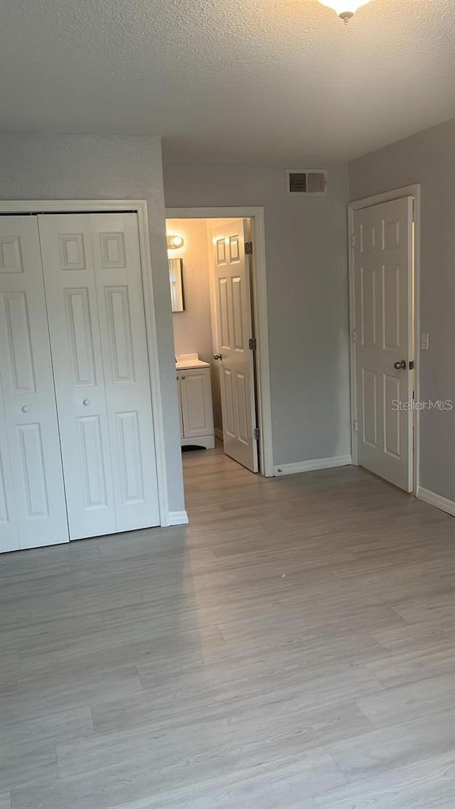 unfurnished bedroom with a textured ceiling, connected bathroom, light hardwood / wood-style flooring, and a closet