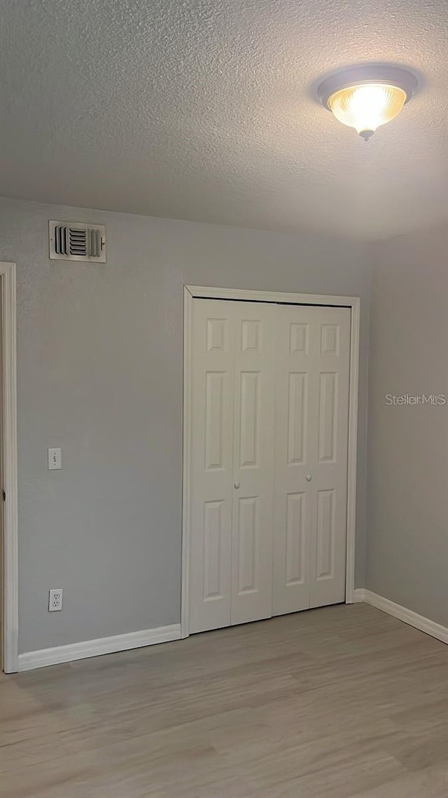 unfurnished bedroom with a textured ceiling, light wood-type flooring, and a closet