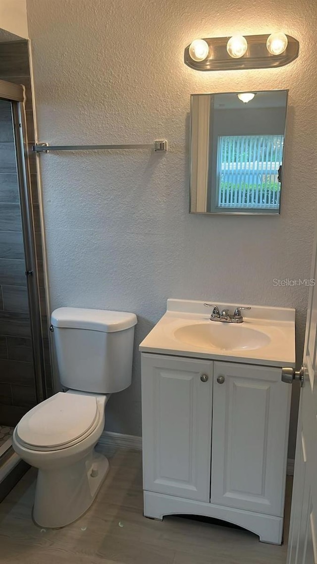 bathroom with wood-type flooring, walk in shower, vanity, and toilet