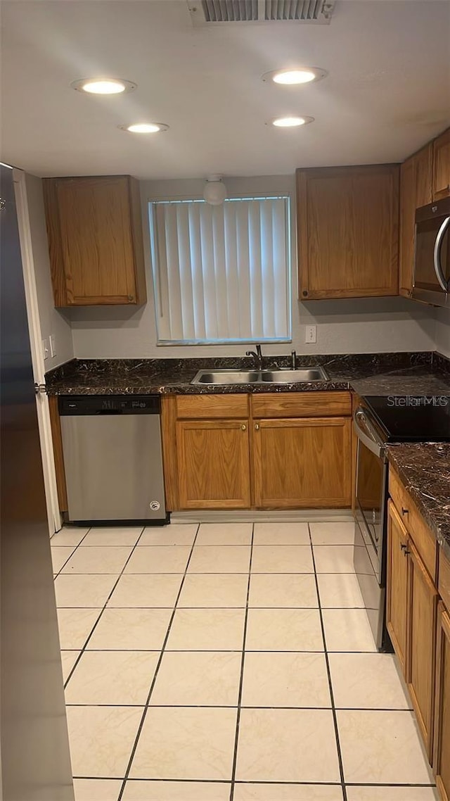 kitchen with dark stone counters, stainless steel appliances, light tile patterned flooring, and sink