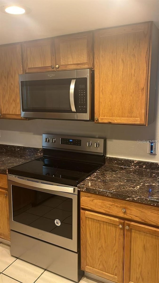 kitchen with dark stone countertops, light tile patterned floors, and stainless steel appliances