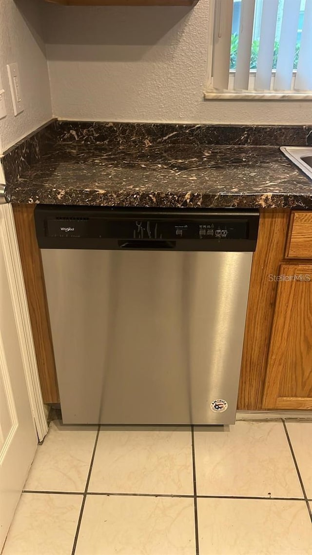 details with dark stone countertops, light tile patterned floors, and stainless steel dishwasher