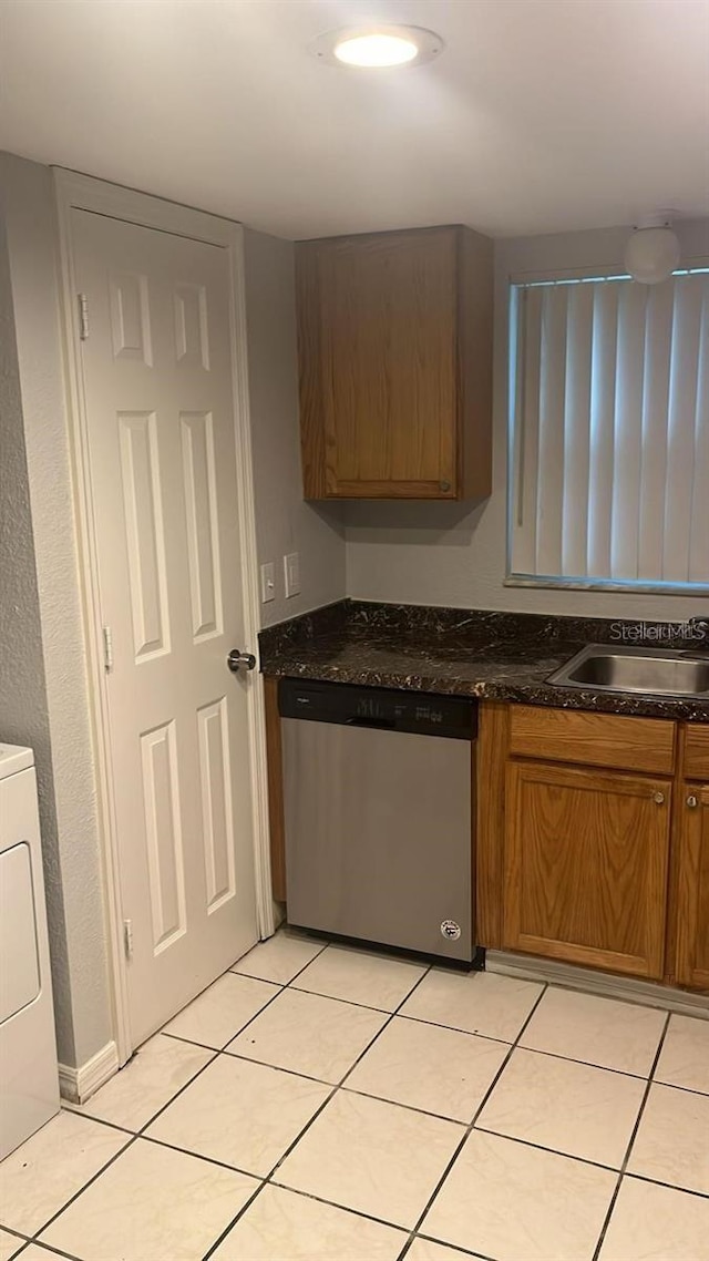 kitchen featuring sink, light tile patterned floors, stainless steel dishwasher, washer / dryer, and dark stone countertops