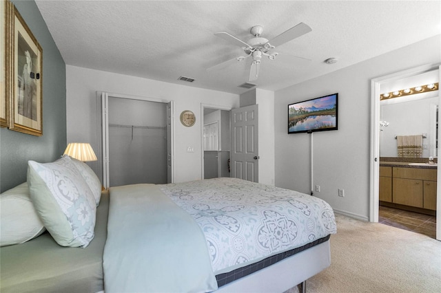 bedroom with light carpet, a textured ceiling, ensuite bathroom, and ceiling fan