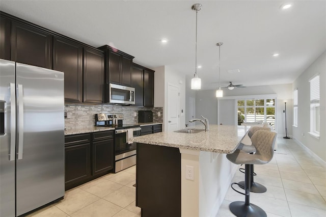 kitchen featuring tasteful backsplash, hanging light fixtures, stainless steel appliances, a center island with sink, and ceiling fan