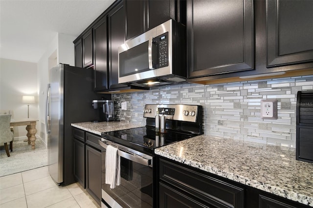 kitchen featuring light stone countertops, stainless steel appliances, backsplash, and light tile patterned flooring