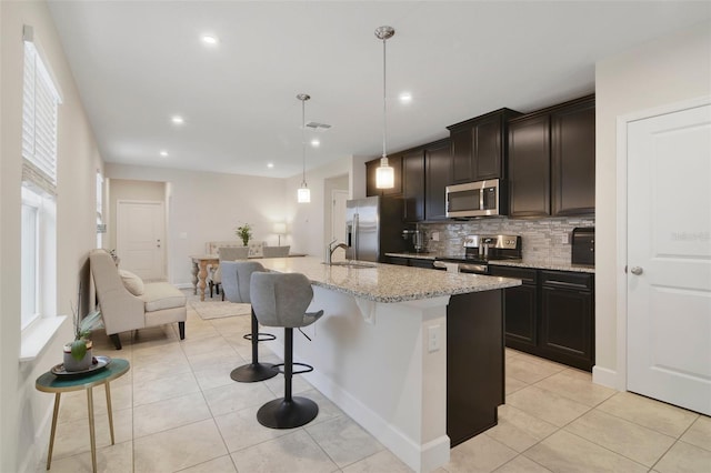 kitchen featuring a breakfast bar, stainless steel appliances, decorative light fixtures, a center island with sink, and sink