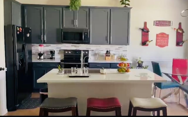 kitchen featuring sink, a kitchen island with sink, black appliances, a kitchen breakfast bar, and decorative backsplash