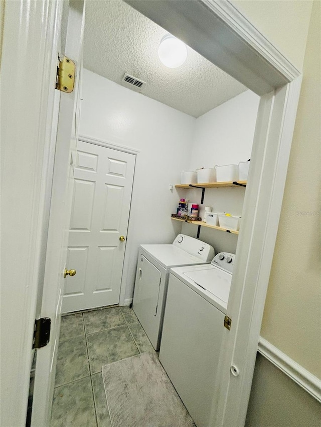 laundry area featuring a textured ceiling, light tile patterned floors, and independent washer and dryer