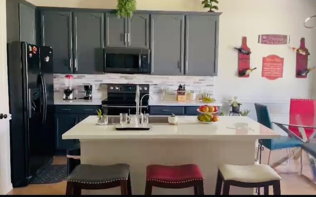 kitchen featuring black appliances, decorative backsplash, sink, and a breakfast bar