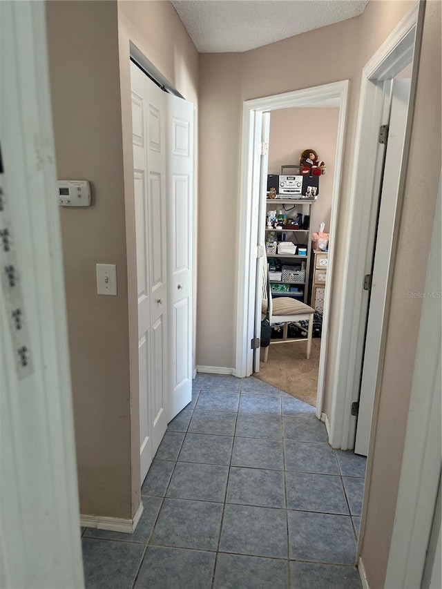 corridor with a textured ceiling and dark tile patterned flooring