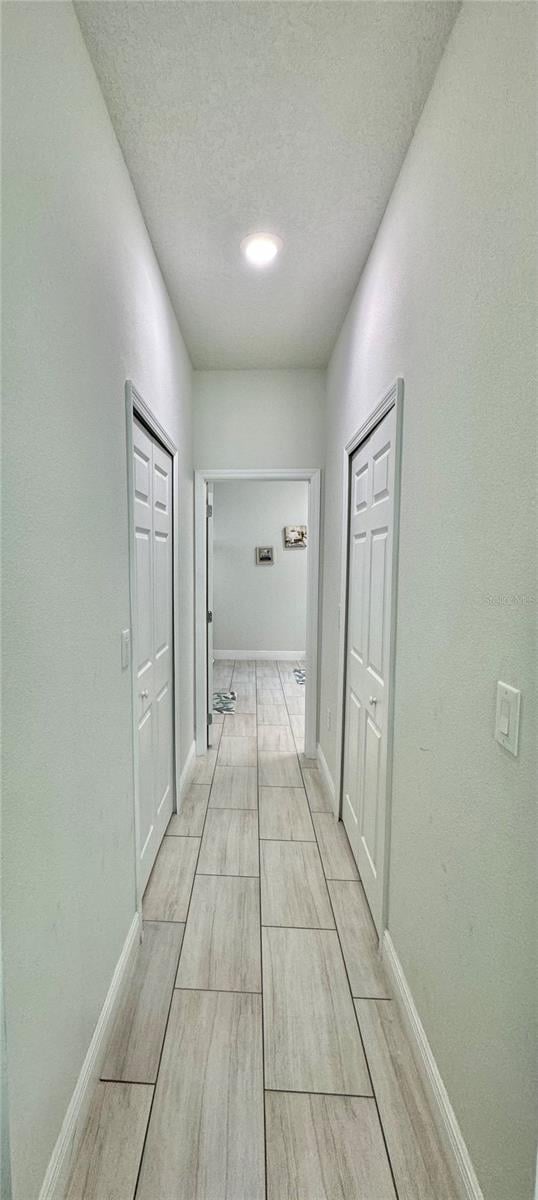 hallway with light wood-type flooring and a textured ceiling