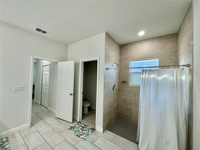 bathroom with a textured ceiling, toilet, and tiled shower