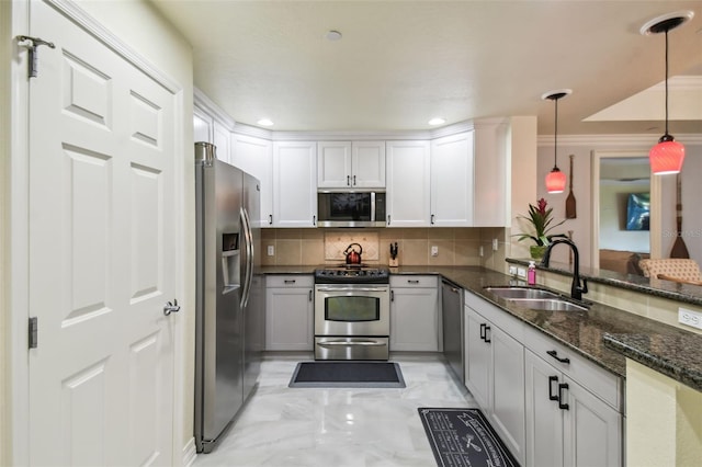 kitchen featuring appliances with stainless steel finishes, dark stone countertops, kitchen peninsula, decorative light fixtures, and sink