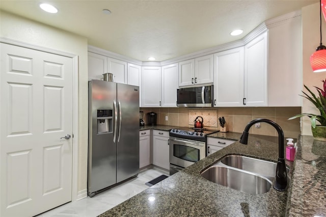 kitchen featuring stainless steel appliances, white cabinets, dark stone countertops, and sink