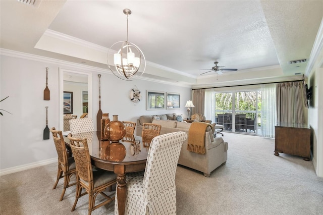 carpeted dining space with ceiling fan with notable chandelier, a tray ceiling, and ornamental molding