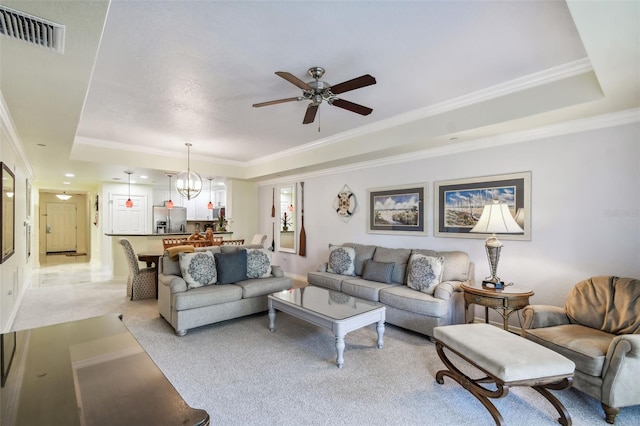 carpeted living room with ceiling fan with notable chandelier, a tray ceiling, and ornamental molding