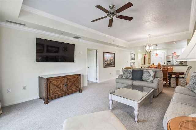 living room with carpet flooring, ceiling fan with notable chandelier, crown molding, and a tray ceiling