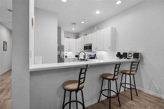 kitchen featuring a breakfast bar, stainless steel appliances, white cabinets, and kitchen peninsula