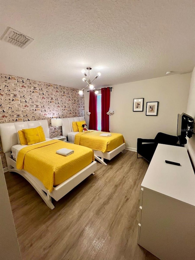 bedroom featuring visible vents, a textured ceiling, wood finished floors, an inviting chandelier, and baseboards