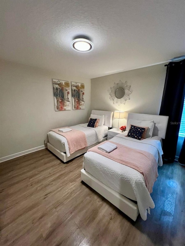 bedroom with a textured ceiling, baseboards, and wood finished floors