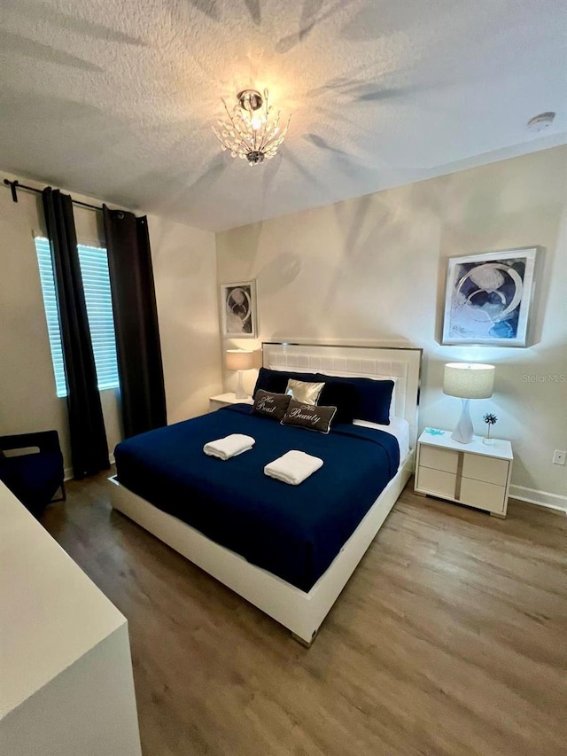 bedroom featuring a textured ceiling, baseboards, and wood finished floors