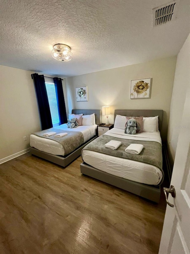 bedroom featuring visible vents, baseboards, a textured ceiling, and wood finished floors