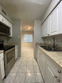 kitchen with sink, appliances with stainless steel finishes, light stone counters, white cabinets, and light tile patterned flooring