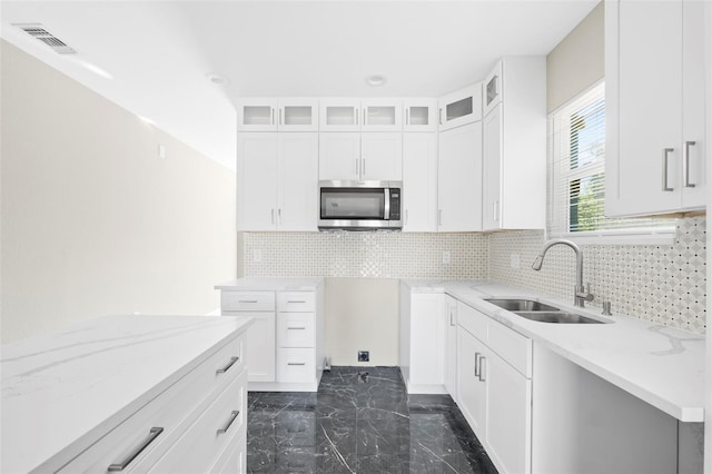 kitchen featuring decorative backsplash, white cabinetry, light stone countertops, and sink