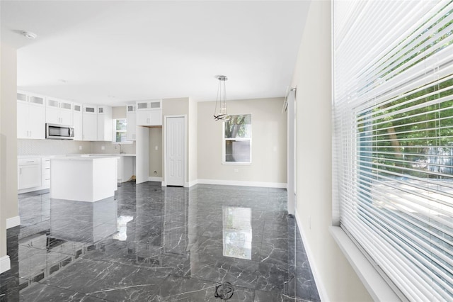 interior space featuring hanging light fixtures, white cabinetry, backsplash, a center island, and sink