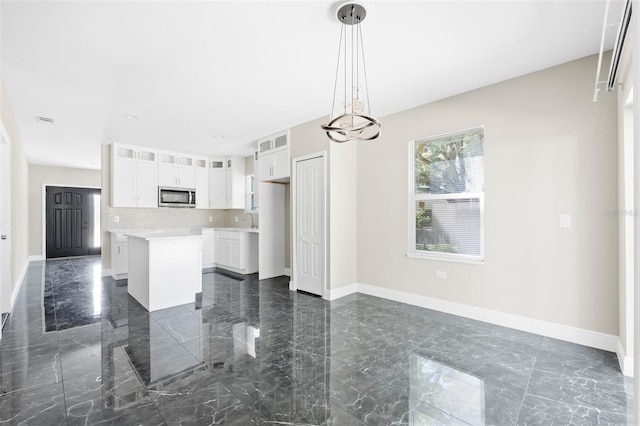 kitchen with sink, white cabinets, hanging light fixtures, a kitchen island, and backsplash