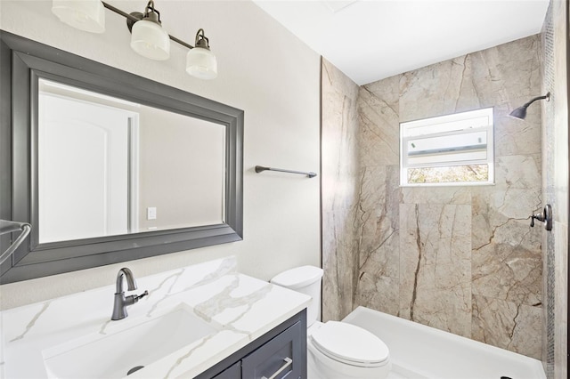 bathroom featuring a tile shower, vanity, and toilet