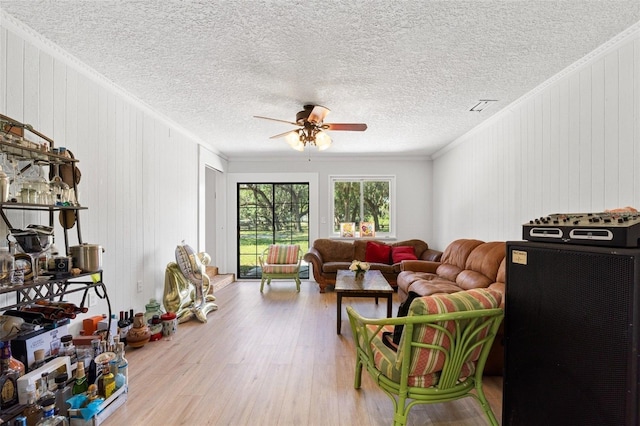 living room with a textured ceiling, light hardwood / wood-style floors, ornamental molding, and ceiling fan