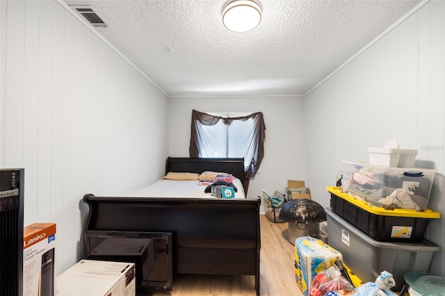 bedroom featuring a textured ceiling, crown molding, wooden walls, and hardwood / wood-style flooring