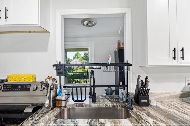 kitchen with stainless steel stove, white cabinets, dark stone counters, and sink