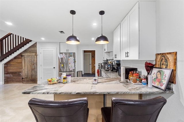 kitchen with light stone counters, stainless steel fridge with ice dispenser, white cabinetry, kitchen peninsula, and a kitchen bar