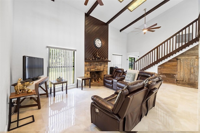 living room with ceiling fan, beamed ceiling, a stone fireplace, wooden walls, and high vaulted ceiling