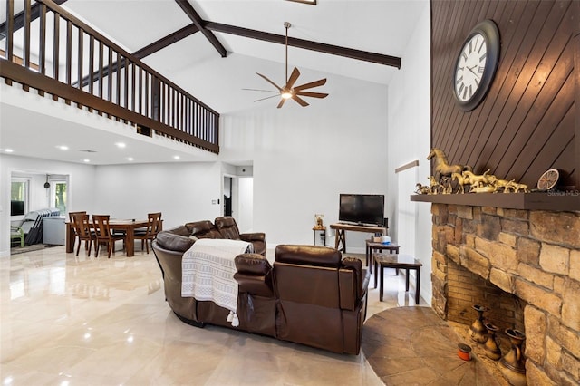 living room with ceiling fan, beamed ceiling, wood walls, high vaulted ceiling, and a fireplace