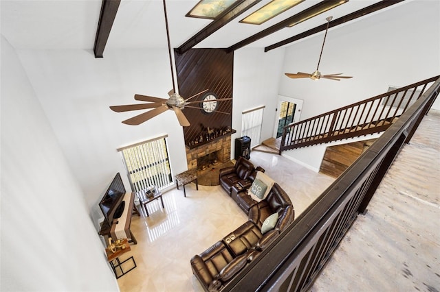 living room featuring ceiling fan, a stone fireplace, and a towering ceiling