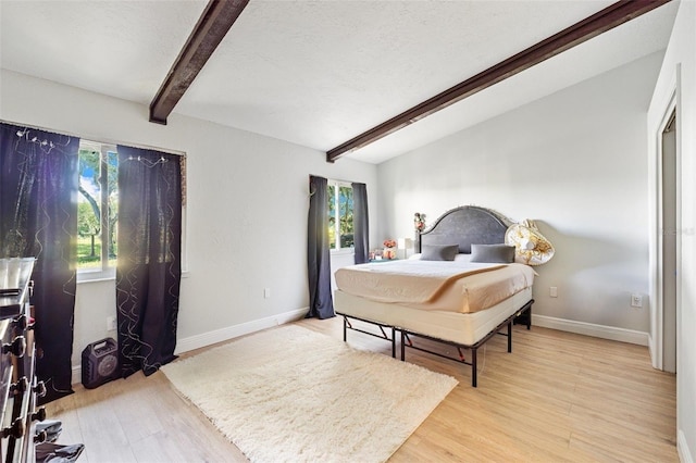 bedroom with lofted ceiling with beams, light wood-type flooring, and multiple windows