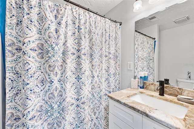 bathroom featuring a textured ceiling, walk in shower, vanity, and toilet