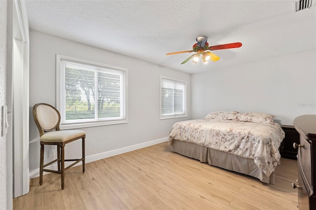 bedroom featuring light hardwood / wood-style floors, ceiling fan, and a textured ceiling