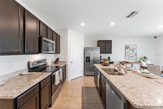 kitchen featuring sink, light tile patterned floors, a textured ceiling, a kitchen island with sink, and appliances with stainless steel finishes