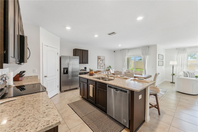 kitchen featuring dark brown cabinets, sink, an island with sink, stainless steel appliances, and light tile patterned floors