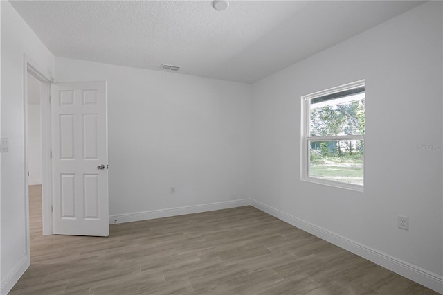 spare room with a textured ceiling and light hardwood / wood-style flooring