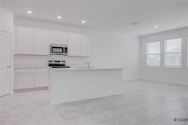 kitchen with appliances with stainless steel finishes, white cabinets, light tile patterned floors, a kitchen island with sink, and sink