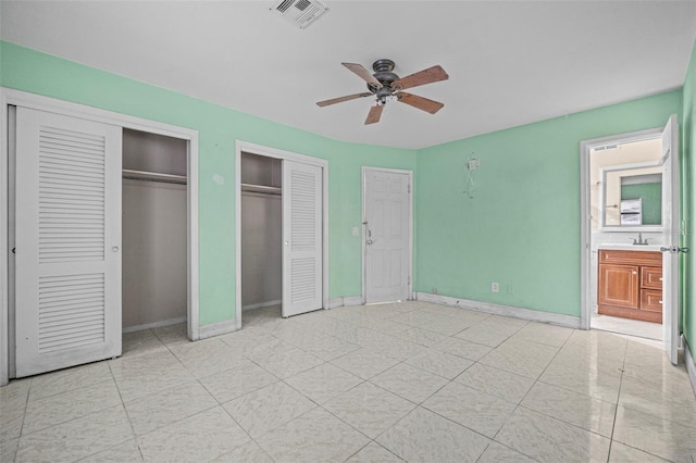 unfurnished bedroom with light tile patterned floors, ceiling fan, two closets, sink, and ensuite bath